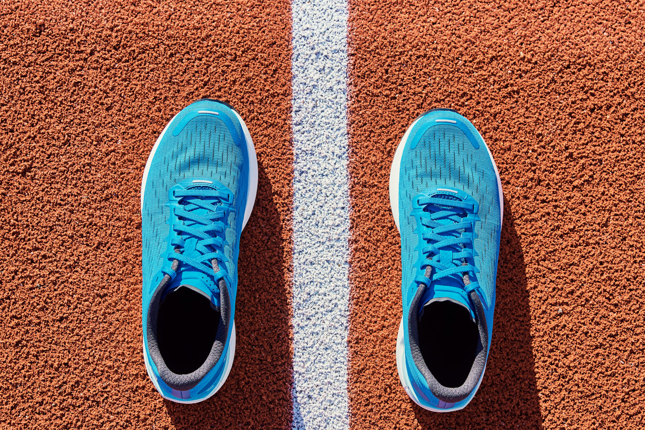 Top view of blue male running sneakers near start line at stadium track.