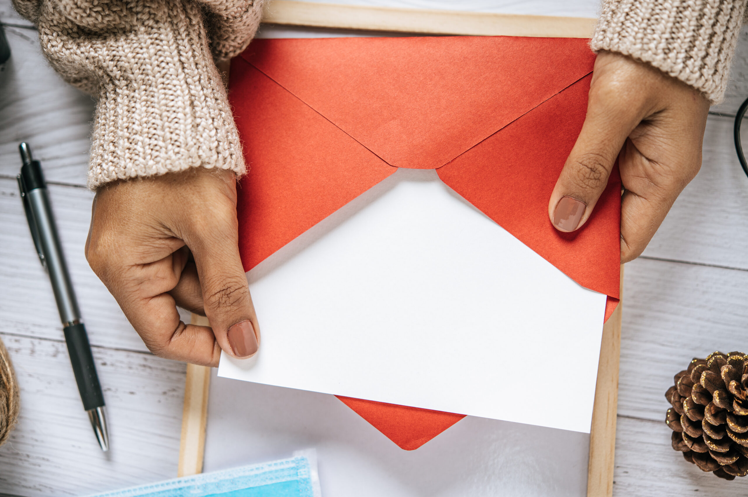 A close-up shot shows a person's hands holding an open red envelope containing a white invitation card.